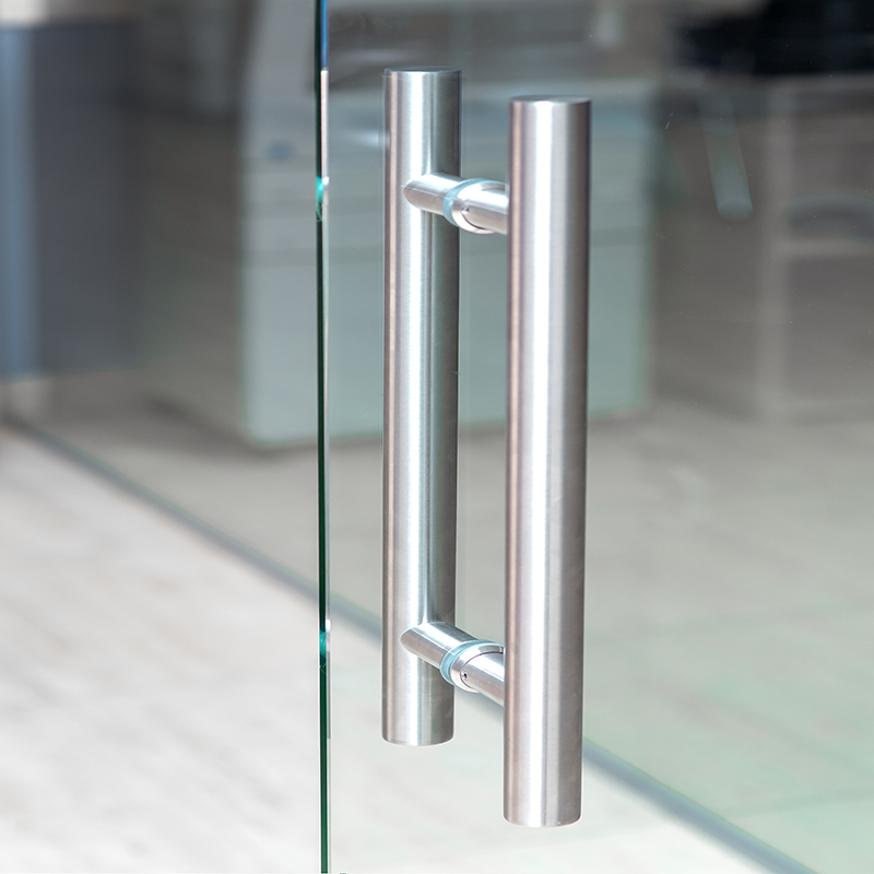 The metal handle of the glass door in the interior of the room, close-up.